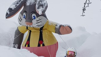 Kind im Schnee mit Hasen-Maskottchen | © Skischule Edelweiß